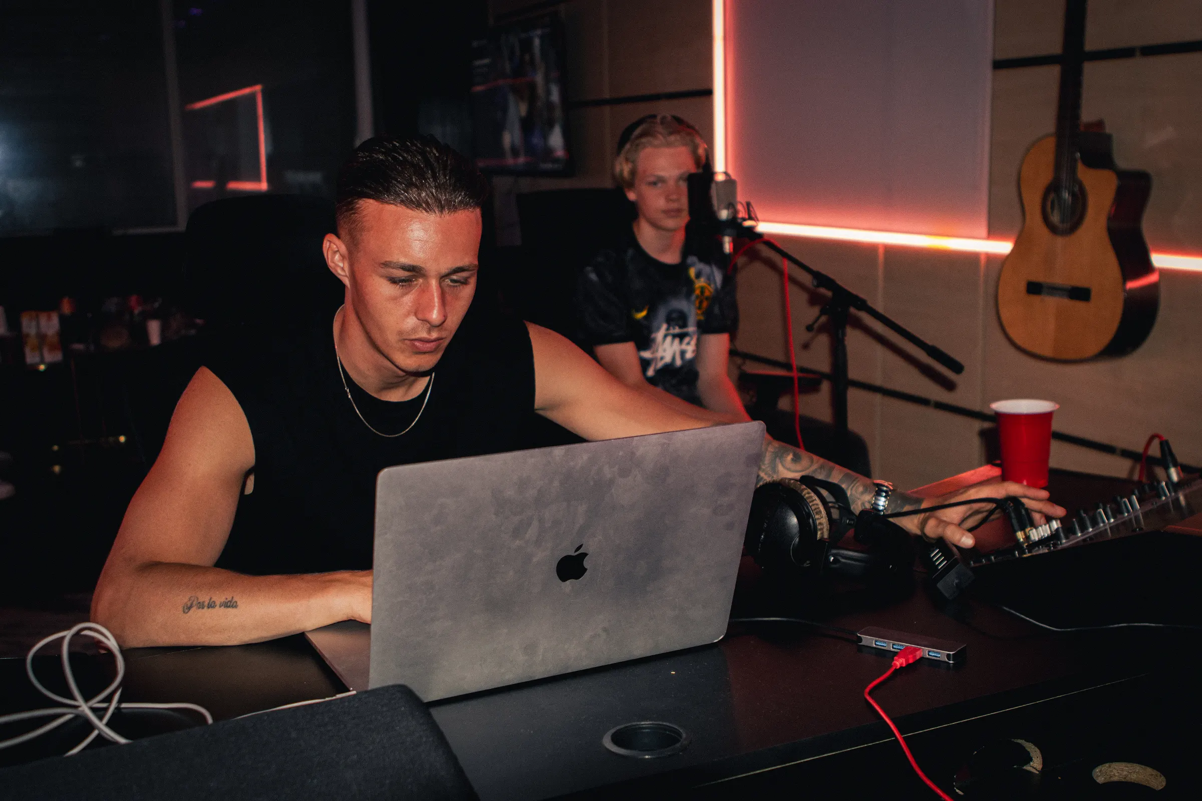 Een producer aan de laptop met een zanger en een meeluisteraar in de studio