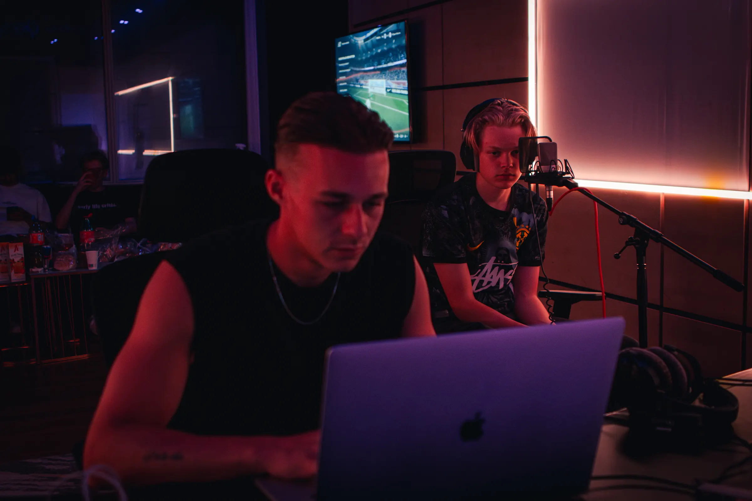 Een producer aan de laptop terwijl een zanger achter hem opneemt